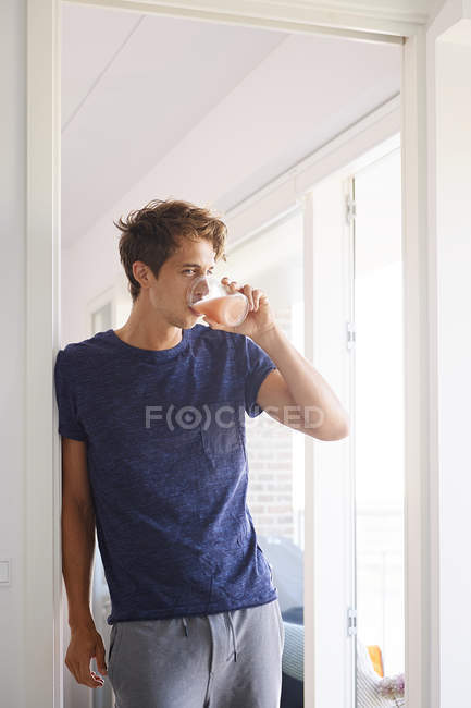 Man leaning against doorway and drinking fruit juice — Stock Photo