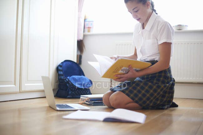 Teenage schoolgirl kneeling on floor looking at book — Stock Photo