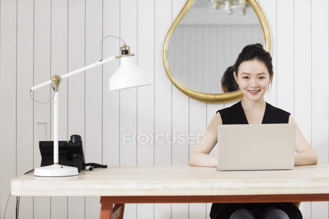 Молода жінка за столом з ноутбуком дивиться на камеру — стокове фото