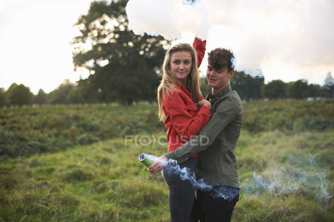 Young couple letting off smoke flares in field — Stock Photo