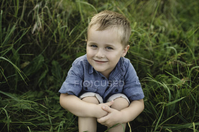 Portrait de garçon souriant assis dans l'herbe haute regardant la caméra — Photo de stock