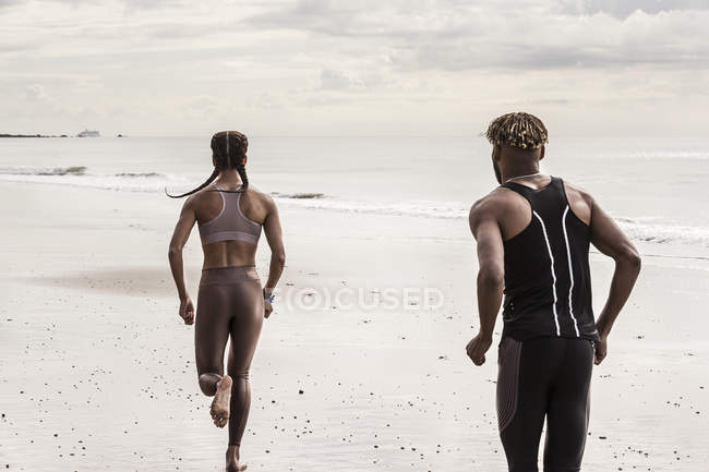 Vista trasera de hombres y mujeres jóvenes corriendo en la playa - foto de stock