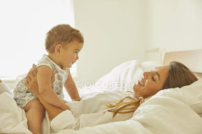 Mãe relaxante na cama com a criança, sorrindo — Fotografia de Stock