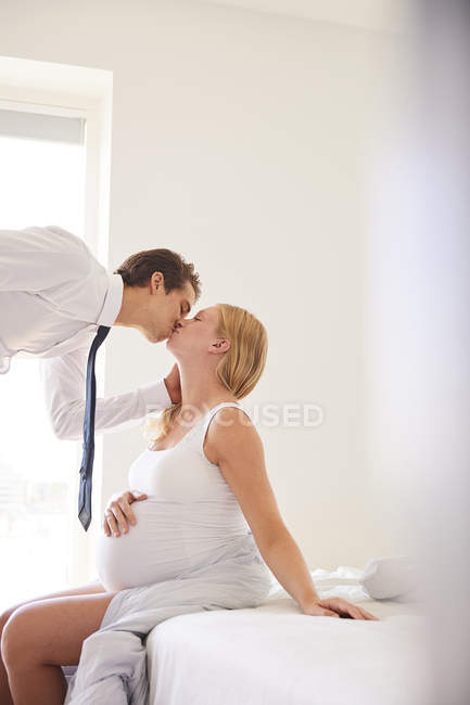 Embarazada mujer besando hombre de negocios marido en el dormitorio - foto de stock