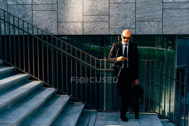 Reifer Geschäftsmann nutzt Smartphone auf Stufen — Stockfoto
