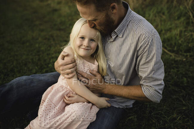 Hija sentada en padres regazo en hierba - foto de stock