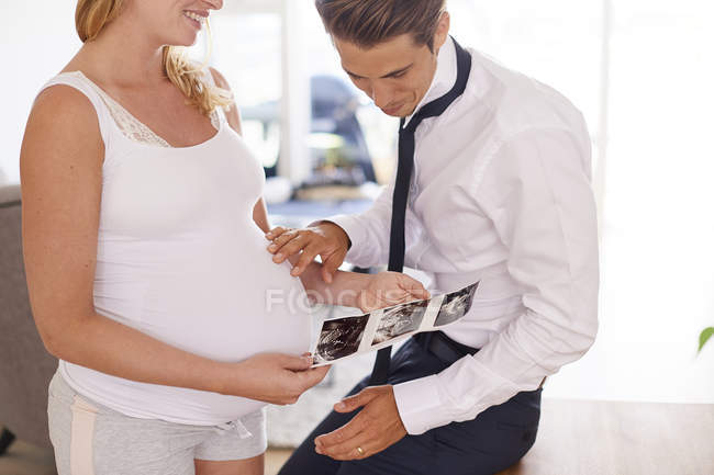 Pareja embarazada mirando imágenes de ultrasonido en la sala de estar - foto de stock
