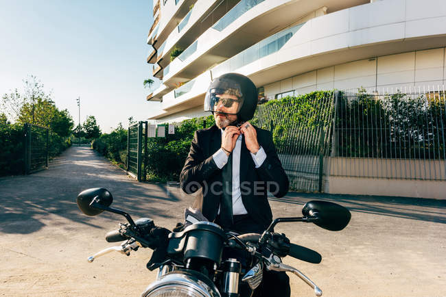 Mature businessman sitting on motorcycle and putting on motorcycle helmet — Stock Photo