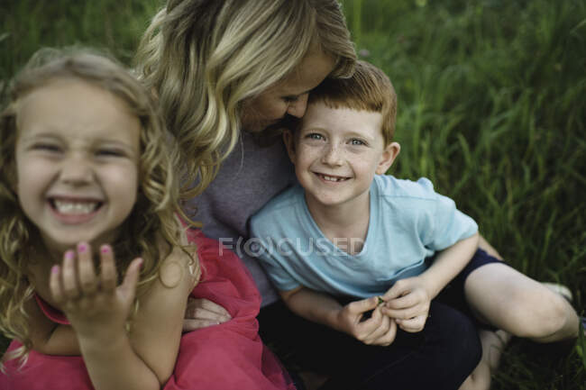 Retrato de niña y hermano sentado en las madres regazo en la hierba - foto de stock