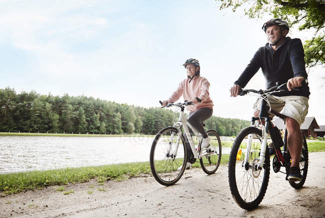 Зріла пара їде на велосипеді по стежці біля озера — стокове фото