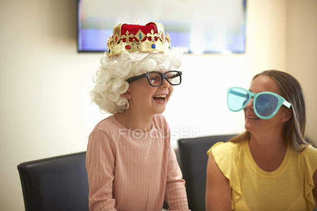 Madre e hija jugando a disfrazarse, usando sombreros y anteojos divertidos, riendo - foto de stock
