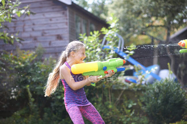 Menina esguichando arma de água no jardim — Fotografia de Stock