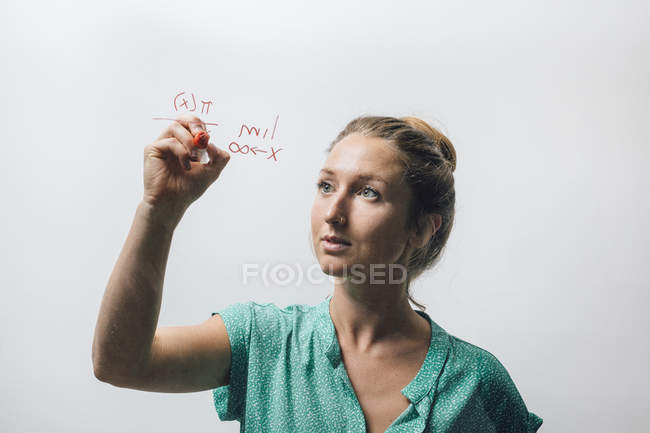 Young woman writing complex equation on glass wall — Stock Photo