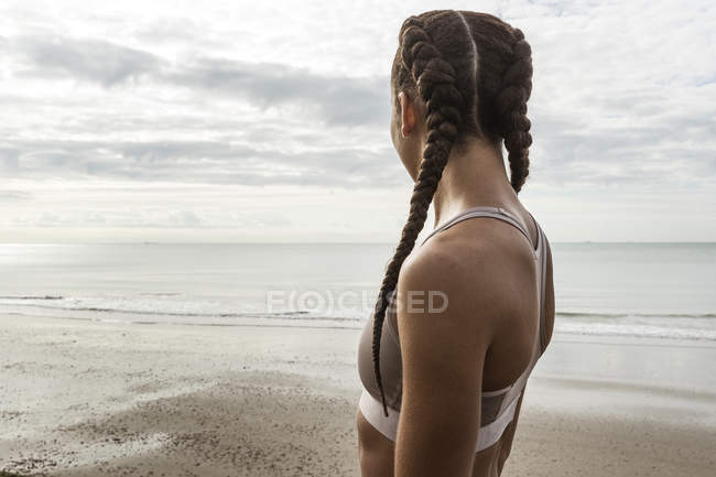 Corredor feminino jovem com tranças de cabelo olhando para o mar — Fotografia de Stock