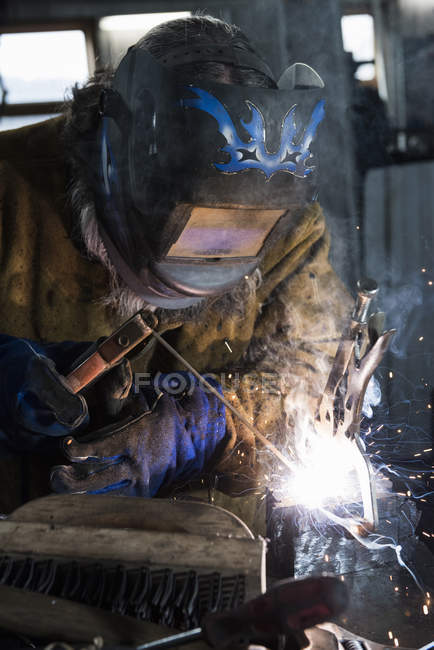 Blacksmith in welding mask welding metal in workshop — Stock Photo