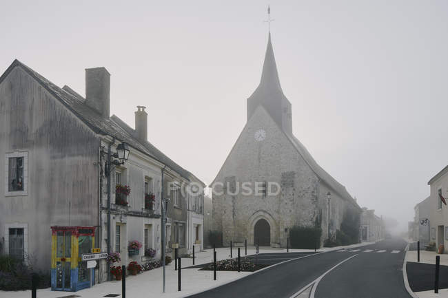 Road and church in Meigne-le-Vicomte village on misty morning, Loire Valley, France — Stock Photo
