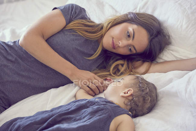 Madre e hija pequeña, acostadas juntas en la cama - foto de stock