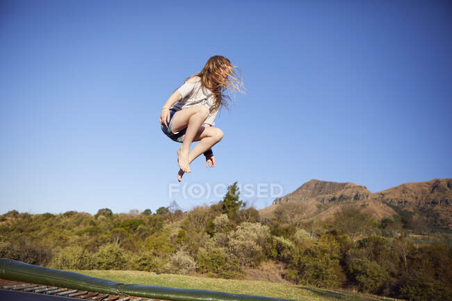 Junges Mädchen springt auf Trampolin, in der Luft, in ländlicher Umgebung — Stockfoto
