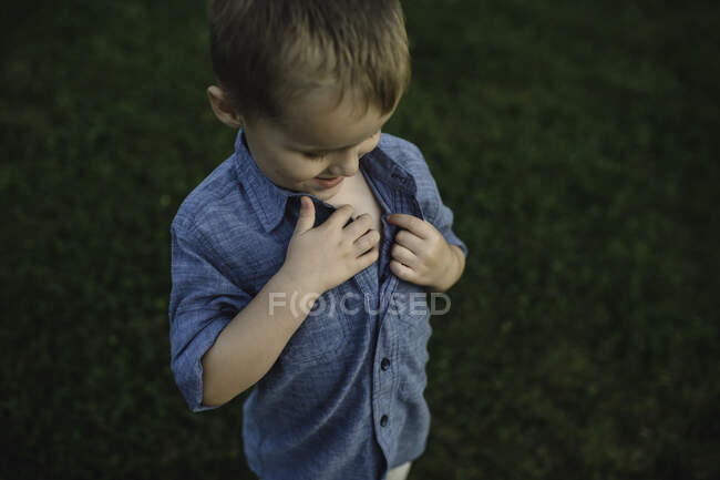 Boy unbuttoning shirt to investigate chest — Stock Photo