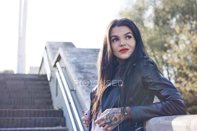 Portrait of young woman leaning against wall, pensive expression, tattoos on hand — Stock Photo