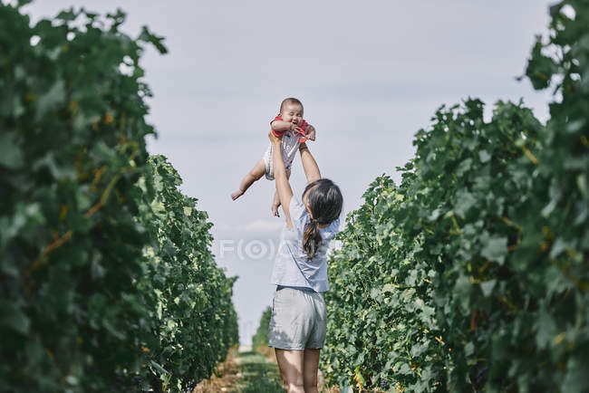 Woman holding up baby daughter in vineyard — Stock Photo