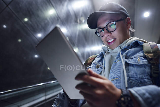 Hombre joven moviéndose por escaleras mecánicas estación subterránea mirando tableta digital - foto de stock