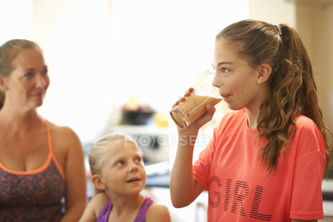 Adolescente chica bebiendo vaso de batido fresco en la cocina - foto de stock