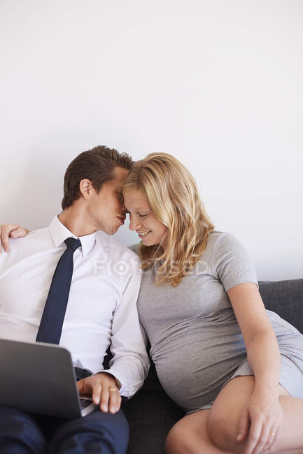 Romantischer Mann flüstert schwangerer Freundin auf Sofa zu — Stockfoto