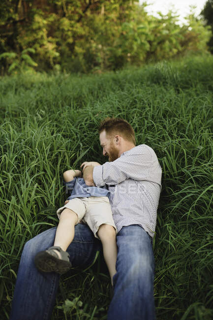 Батько лоскоче сина в високій траві — стокове фото