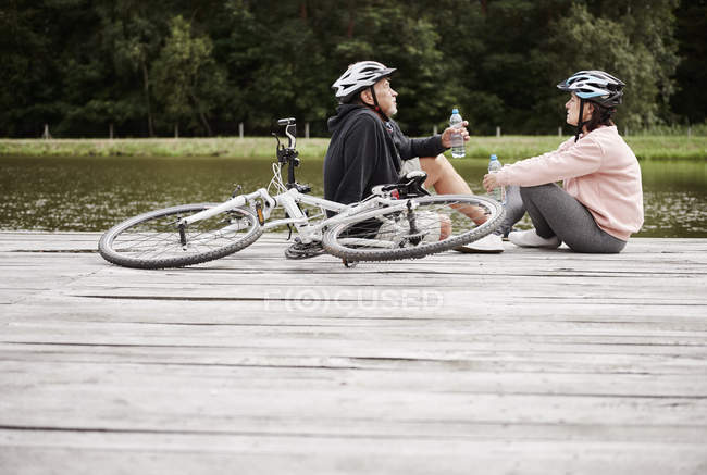 Mature couple with bicycles relaxing on pier beside lake — Stock Photo