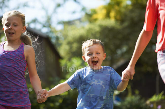 Hermanos tomados de la mano corriendo en el jardín - foto de stock