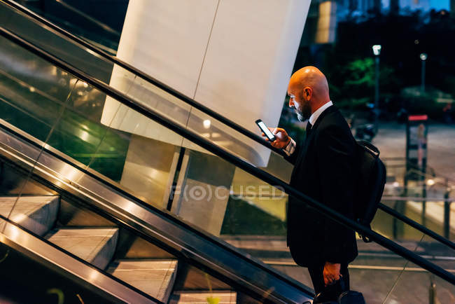 Mature businessman using smartphone on escalator — Stock Photo