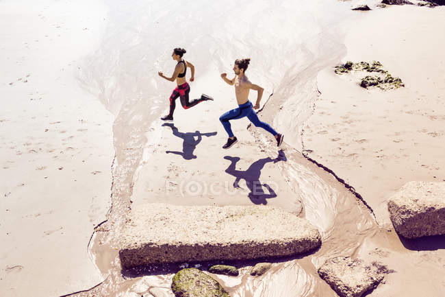 Возвышенный вид молодых мужчин и женщин, бегущих вдоль пляжа — стоковое фото