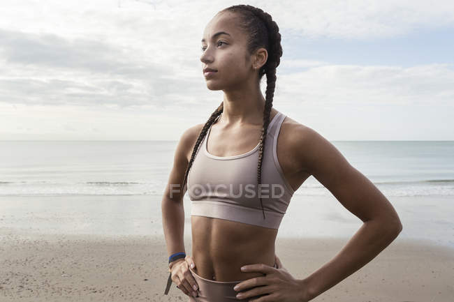 Junge Läuferin mit den Händen auf den Hüften am Strand — Stockfoto