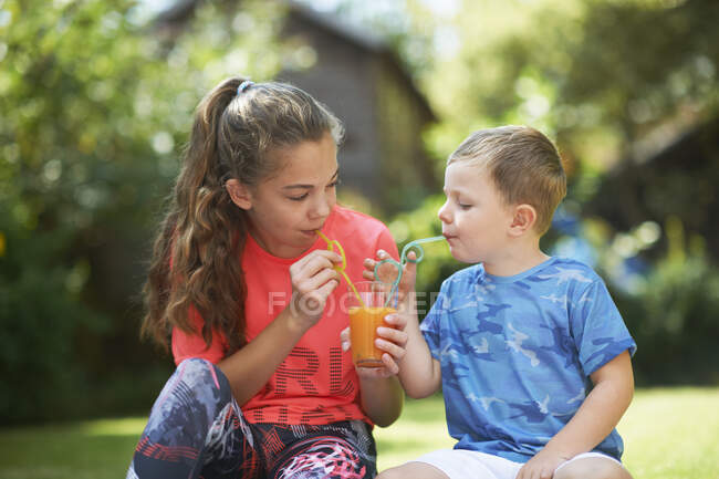Teenage girl and brother sharing fresh smoothie in garden — Stock Photo