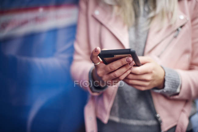Mid section of young woman holding smartphone at city tram station — Stock Photo