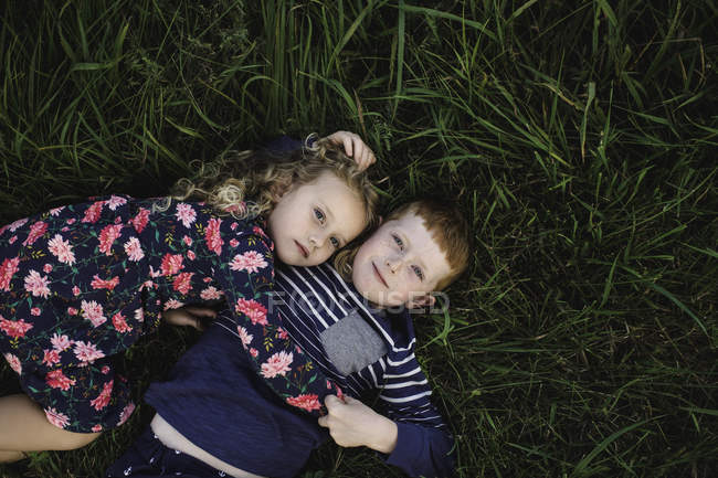 Overhead portrait of boy and sister lying on grass hugging — Stock Photo