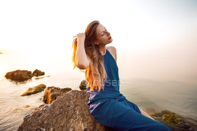 Молода жінка сидить на пляжному камені з рукою в довге волосся — стокове фото