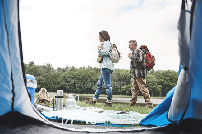 Casal maduro andando com mochilas perto de barraca aberta — Fotografia de Stock