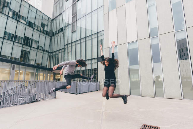 Молода пара в міському середовищі, стрибає з радістю — стокове фото