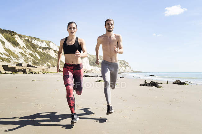 Giovane uomo e donna che corrono lungo la spiaggia — Foto stock
