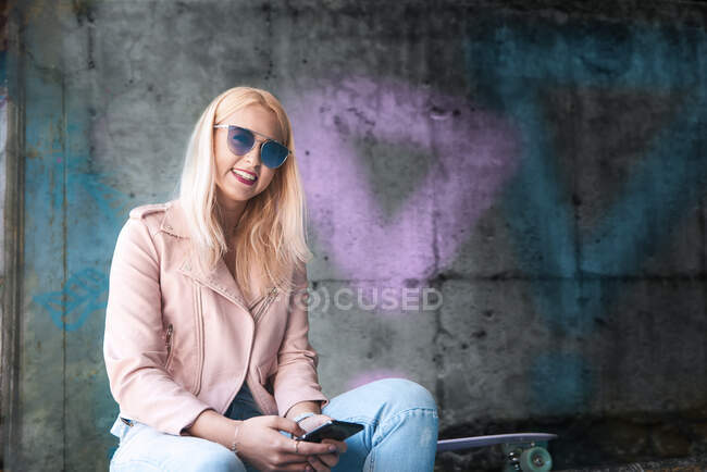 Portrait of young blond female skateboarder wearing sunglasses at skateboard park — Stock Photo