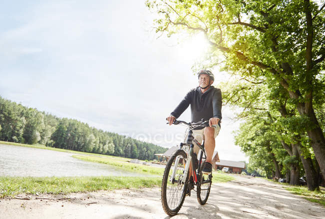 Uomo anziano in bicicletta sul sentiero vicino al lago — Foto stock