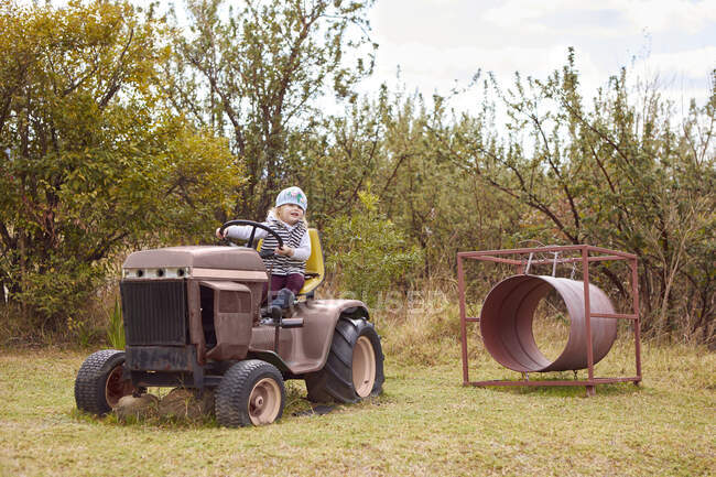 Giovane ragazza seduta sul trattore, in ambiente rurale — Foto stock