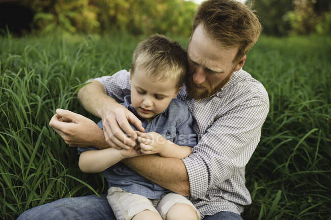 Father and son sitting in tall grass investigating nature — Stock Photo