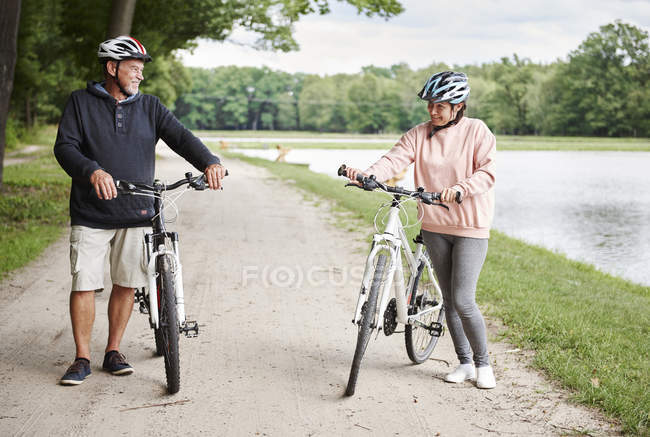 Casal maduro caminhando ao longo do caminho rural com bicicletas — Fotografia de Stock