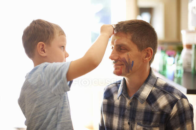 Junge zeichnet mit Kinderschminke auf das Gesicht des Vaters — Stockfoto