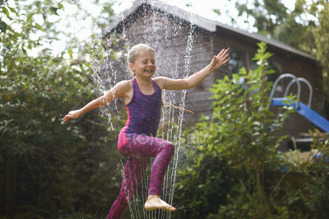 Девушка прыгает через сад разбрызгиватель — стоковое фото