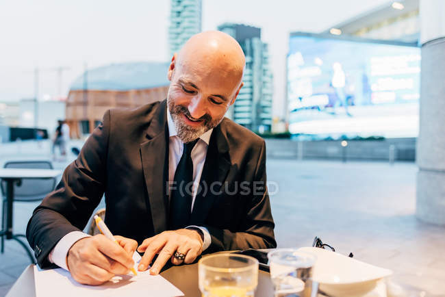 Зрілий бізнесмен підписує документ у відкритому кафе — стокове фото