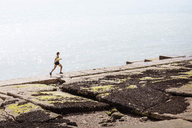 Jovem mulher correndo ao longo da parede do mar — Fotografia de Stock